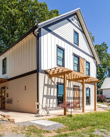 Barndo 3 exterior with white board-and-batten siding, black trim, wooden pergola, and summer greenery in New Market, Tennessee