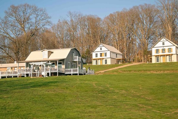 Modernes Farmhaus mit weiß-schwarzer Fassade, Holzpergolen und Sitzplätzen auf der Terrasse, umgeben von alten Bäumen