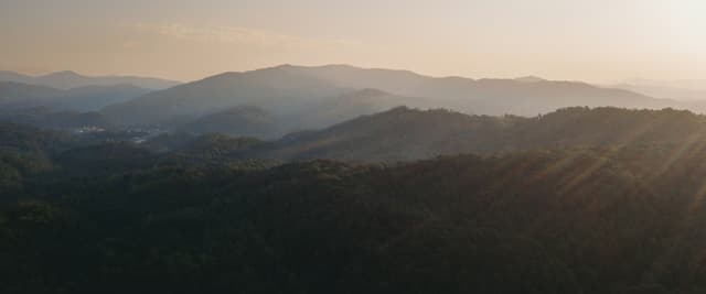 Sunset light rays breaking over the Great Smoky Mountains ridgeline, viewed from an aerial vantage above forested hills